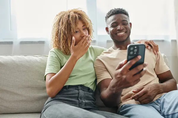 Счастливая африканская американская пара смеется в то время как видео чате на смартфоне дома, общение — стоковое фото