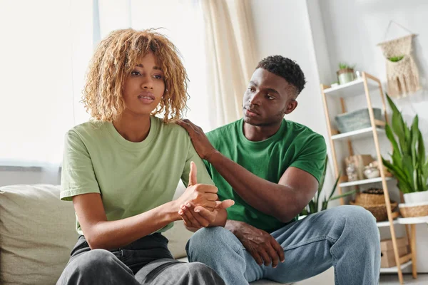 Young african american man comforting girlfriend in braces showing help sign, emotional support — Stock Photo