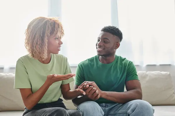Glückliche Afroamerikanerin, die mit Gebärdensprache kommuniziert, während sie mit einem Mann auf der Couch sitzt — Stockfoto
