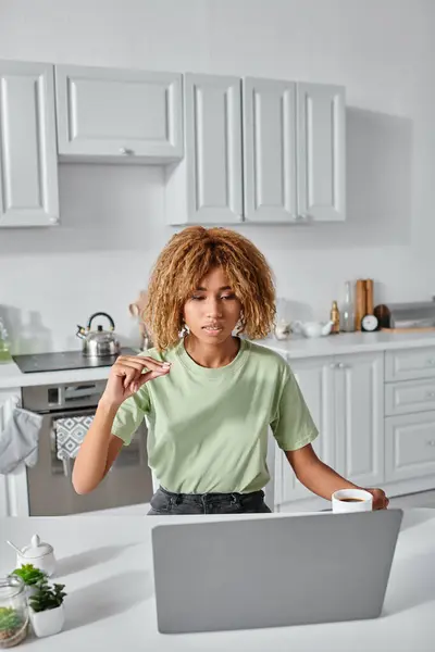 Focused african american woman using sign language during video call and holding cup of coffee — Stock Photo
