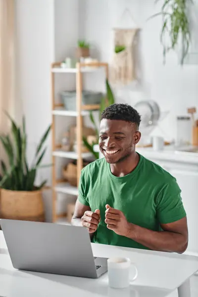 Hombre afroamericano sonriendo mientras se utiliza el lenguaje de señas durante la videollamada en el ordenador portátil en casa - foto de stock