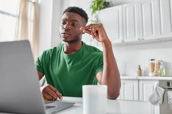 Hombre afroamericano enfocado utilizando lenguaje de señas durante la videollamada en el ordenador portátil en casa, trabajo remoto - foto de stock