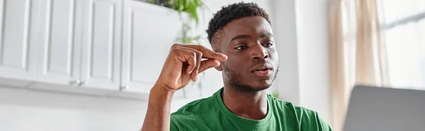 Зосереджений афроамериканський чоловік використовує мову жестів під час відеодзвінка на ноутбуці вдома, банер — стокове фото
