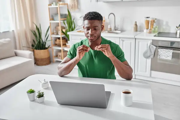 Joven afroamericano sordo utilizando el lenguaje de señas durante la videollamada en el ordenador portátil en casa - foto de stock