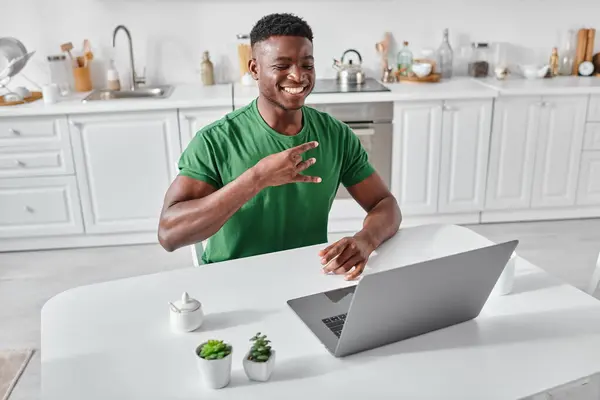 Щасливий глухий афроамериканський фрілансер, використовуючи мову жестів під час відеодзвінка на ноутбуці вдома — стокове фото