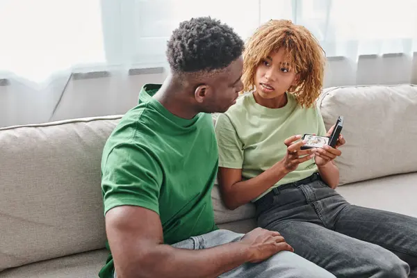 Deaf african american woman holding hearing aid in a box near boyfriend while sitting on couch — Stock Photo
