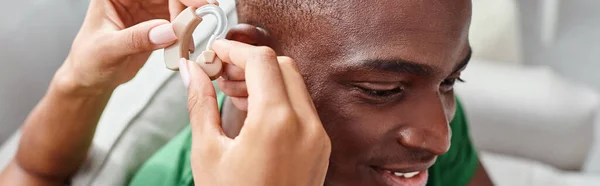 Afro-americano homem sorrindo como sua namorada auxilia com aparelho auditivo, equipamento médico bandeira — Fotografia de Stock