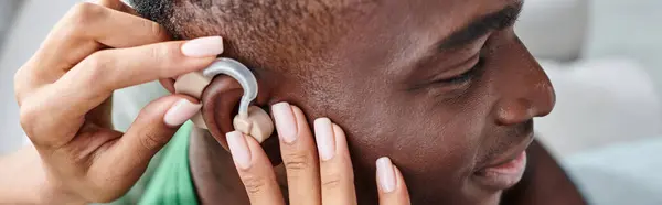 Щасливий афроамериканський чоловік посміхається, коли його дівчина допомагає з слуховим апаратом, медичний банер — Stock Photo