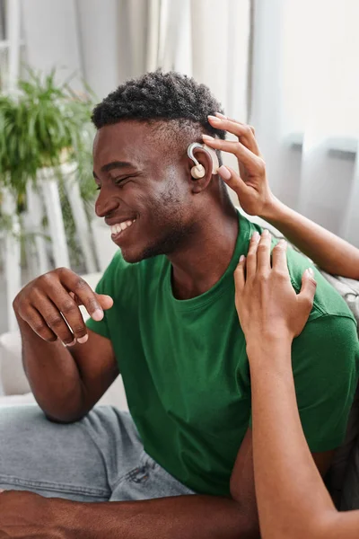 Alegre afro-americano homem sorrindo como sua namorada auxilia com aparelho auditivo, equipamentos médicos — Fotografia de Stock