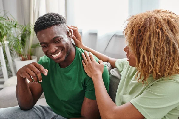 Hombre afroamericano sonriendo como su novia rizada ayuda con audífonos, equipo médico - foto de stock