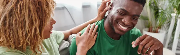 Афроамериканський чоловік посміхається, як його кучеряве подруга допомагає з слуховим апаратом, горизонтальний банер — Stock Photo