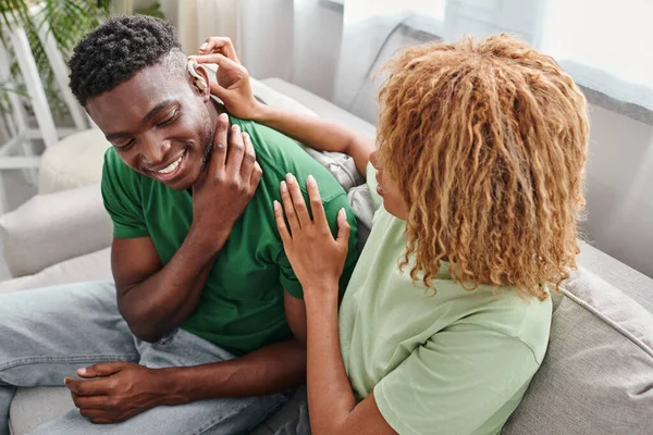Deaf african american man smiling as his curly girlfriend assists with hearing aid, medical device — Stock Photo