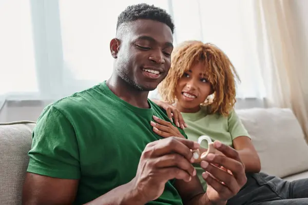 Feliz homem americano africano segurando aparelho auditivo dispositivo médico perto da namorada, dispositivo de escuta — Fotografia de Stock