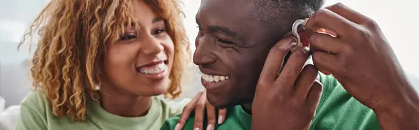 Deaf and happy african american man wearing hearing aid near girlfriend, health device banner — Stock Photo