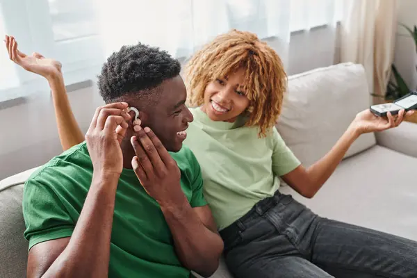 Глухой и счастливый африканский американец носит слуховой аппарат рядом с веселой подругой, устройство для здоровья — стоковое фото
