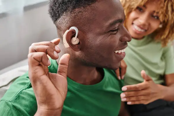 Збуджений афроамериканський чоловік у пристрої слухового апарату, що сидить біля розмитої дівчини в дужках — стокове фото