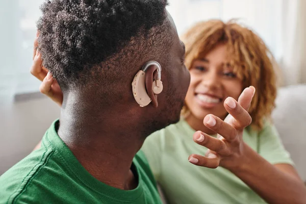 Uomo afroamericano in apparecchio acustico seduto vicino alla fidanzata offuscata, attrezzatura medica — Foto stock