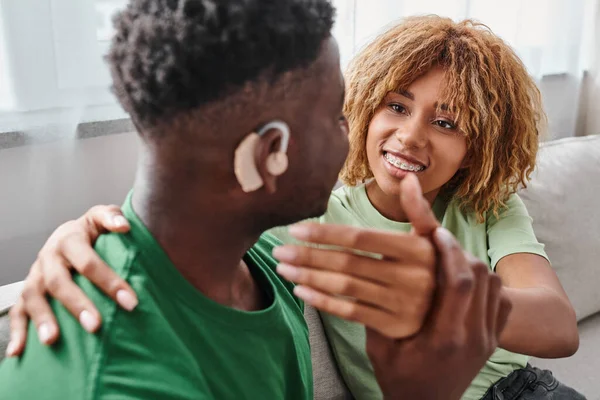 Mujer afroamericana feliz abrazando novio en dispositivo de audífono, equipo médico - foto de stock