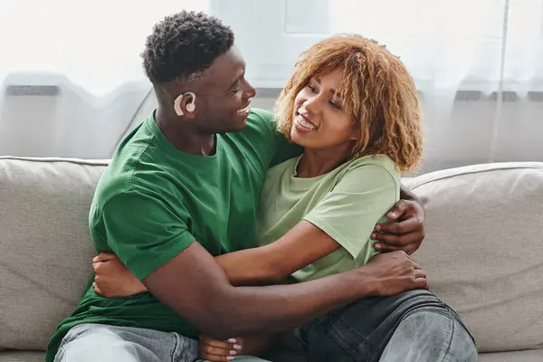 Happy African American couple embracing on couch, deaf black man in hearing aid and woman in braces — Stock Photo