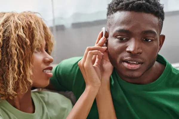 Encaracolado Africano americano mulher segurando aparelho auditivo dispositivo médico perto namorado, acessibilidade — Fotografia de Stock