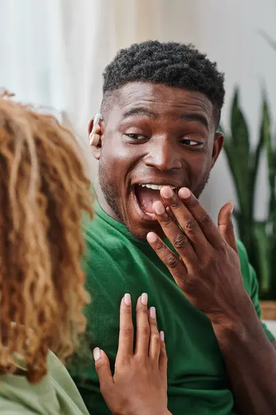 Eccitato uomo africano americano in apparecchio acustico dispositivo sorridente felicemente vicino fidanzata a casa — Foto stock