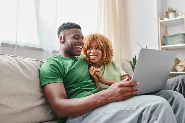 Alegre casal afro-americano andando filme no laptop, homem surdo em ouvir ar e mulher no aparelho — Fotografia de Stock
