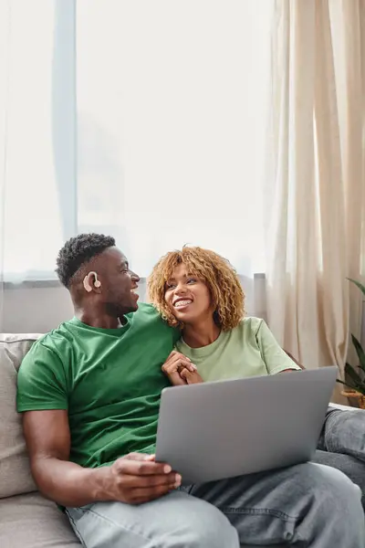 Cheerful african american couple walking movie on laptop, deaf man in hearing air and woman — Stock Photo
