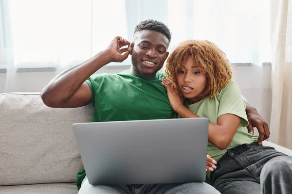 Cheerful black couple walking movie on laptop, deaf man in hearing air and woman in braces — Stock Photo