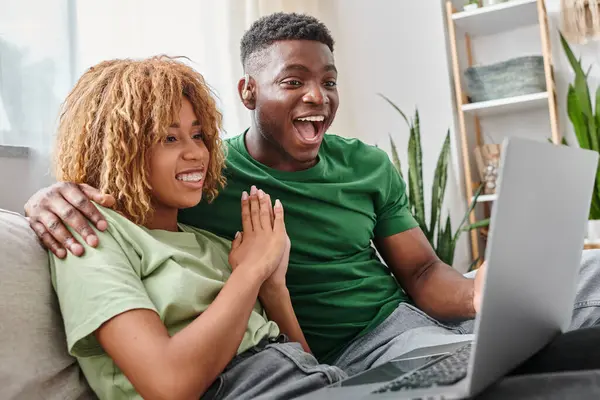 Збуджений афроамериканський чоловік у слуховому апараті дивиться фільм на ноутбук з дівчиною — Stock Photo
