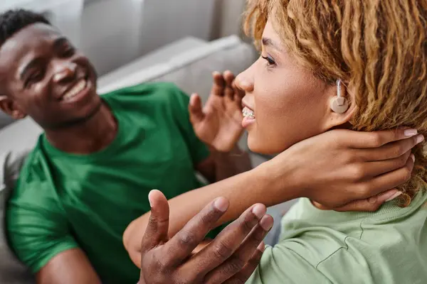 Portrait of deaf african american woman in hearing aid device smiling near boyfriend at home — Stock Photo