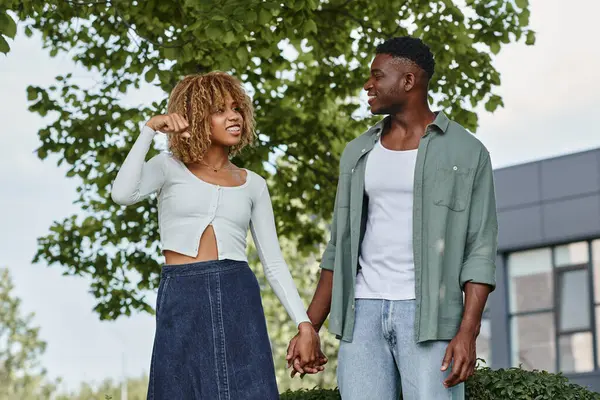 Joven pareja afroamericana cogida de la mano y comunicándose con gestos de la mano al aire libre - foto de stock