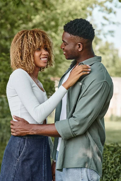 Glückliches afrikanisch-amerikanisches Paar hält Händchen und umarmt sich im Freien, Frau in Hosenträgern — Stockfoto