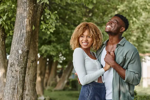 Alegre casal afro-americano de mãos dadas e abraçando uns aos outros ao ar livre, mulher de aparelho — Fotografia de Stock