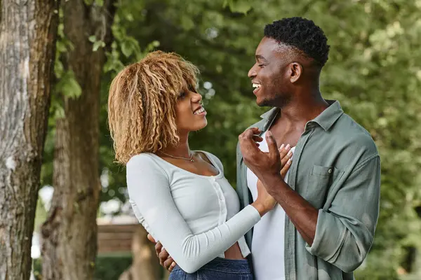 Complacida pareja afroamericana abrazándose y sonriendo al aire libre, mujer con frenillos - foto de stock