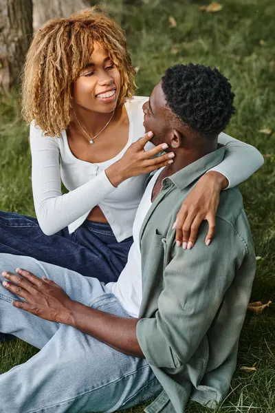 Happy african american woman in casual wear touching face of boyfriend and sitting on grass, banner — Stock Photo
