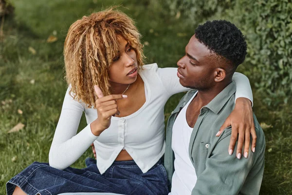 Young african american couple using sign language for communication while sitting on grass — Stock Photo