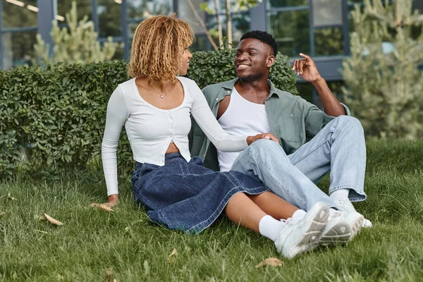 Feliz africano americano pareja usando el lenguaje de señas para la comunicación mientras está sentado en la hierba - foto de stock