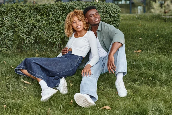 Весела афроамериканська пара обіймає і сидить разом на зеленій траві, щастя — стокове фото