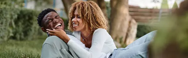 Striscione di felice donna afro-americana che condivide uno sguardo amorevole mentre siede su un'erba con l'uomo — Foto stock