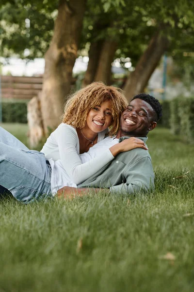 Cheerful african american couple having quality time with each other while lying on grass — Stock Photo