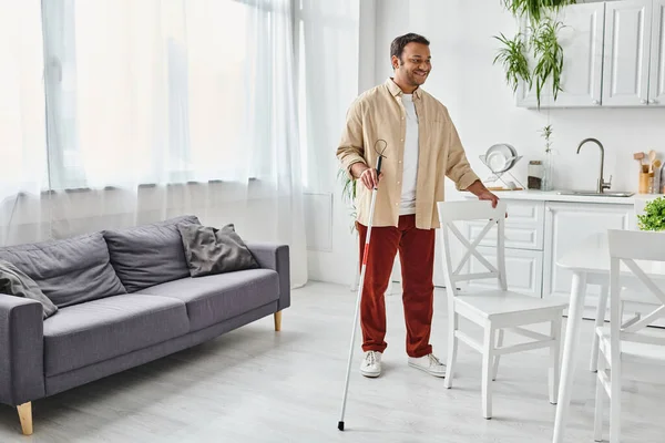 Cheerful indian man with visual impairment in casual attire using walking stick while at home — Stock Photo