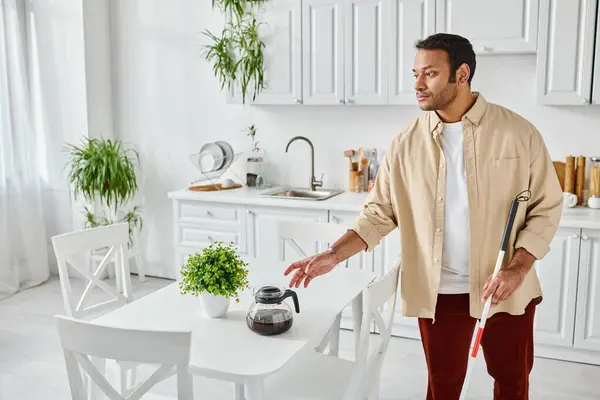 Attractive indian man with blindness using walking stick and holding coffee pot while in kitchen — Stock Photo