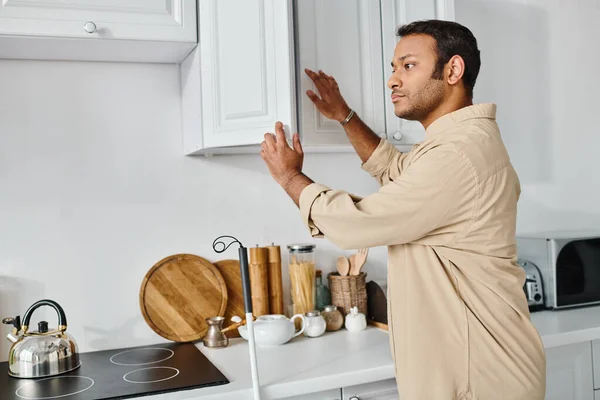 Handsome indian disabled man in casual attire with walking stick reaching products on kitchen — Stock Photo