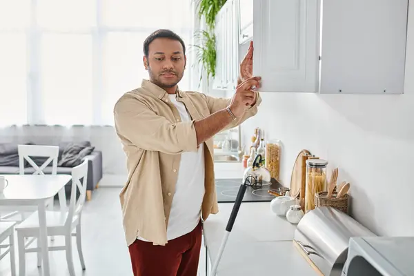 Attractive indian disabled man in casual attire with walking stick reaching products on kitchen — Stock Photo