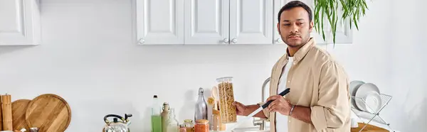 Bell'uomo indiano con cecità in abito casual raccogliendo barattolo di maccheroni mentre in cucina, banner — Foto stock