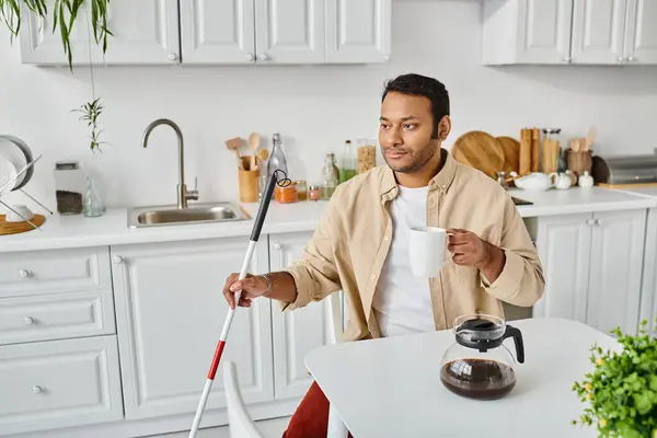 Good looking indian man with visual impairment sitting and drinking tasty coffee while on kitchen — Stock Photo