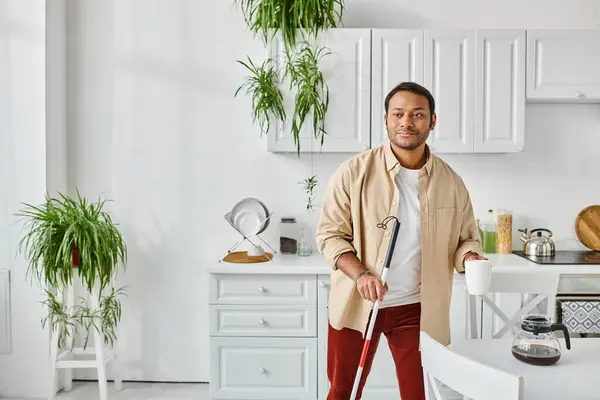 Attractive disabled indian man in cozy homewear with walking stick holding coffee cup on kitchen — Stock Photo