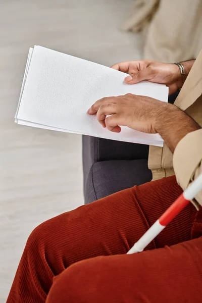 Cropped view of indian blind man in casual clothing sitting on sofa and reading braille code — Stock Photo
