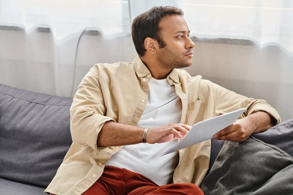 Good looking indian man with blindness in cozy clothing sitting on sofa and reading braille code — Stock Photo