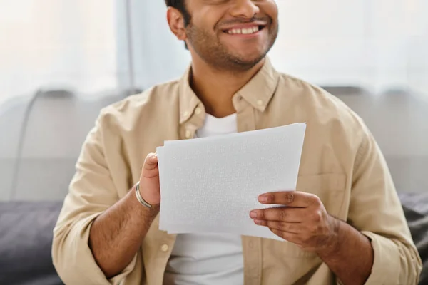 Joyful indian blind man in casual comfortable attire sitting on sofa and reading braille code — Stock Photo
